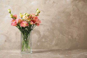 Eustoma flowers in vase on table near beige wall, space for text