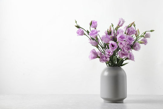 Eustoma flowers in vase on table near white wall, space for text