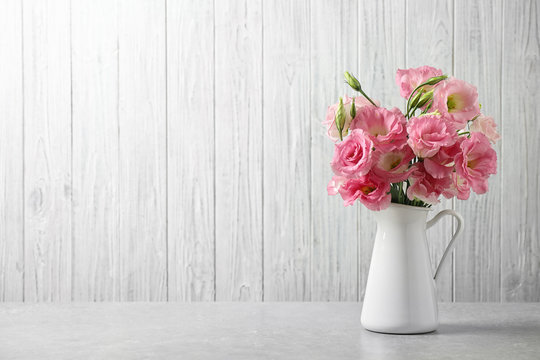 Eustoma flowers in vase on table near white wall, space for text