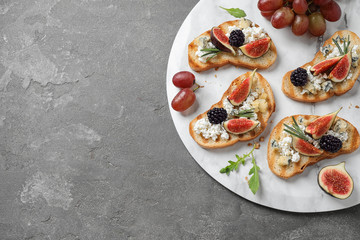 Bruschettas with cheese, figs and blackberries served on grey table, top view. Space for text