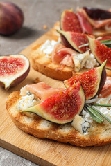 Fototapeta na wymiar Bruschettas with cheese, prosciutto and figs served on wooden board, closeup