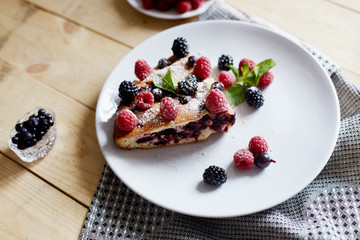 Piece of pie with blueberries, rasberry and mint for dessert on a white plate, napkin. Pieces of delicious homemade cake on a wooden boards background