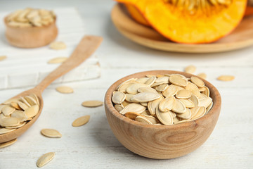 Bowl of raw pumpkin seeds on white wooden table