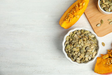 Flat lay composition with raw pumpkin seeds on white wooden table, space for text