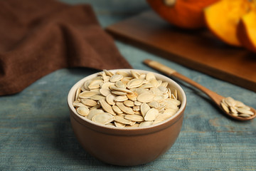 Fototapeta premium Bowl of raw pumpkin seeds on blue wooden table
