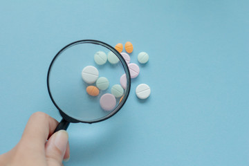 Magnifying glass with pills on blue background. pharmaceutical inspection identifies pills. Medicinal substance quality concept.