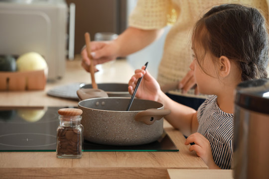 Little Daughter With Mother Cooking Soup In Kitchen