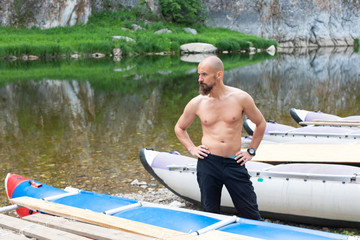 bearded man with a naked torso standing on the shore near the boats, waiting for departure. .summer...