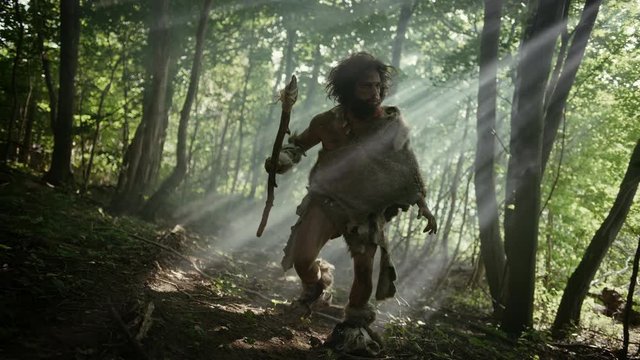 Portrait of Primeval Caveman Wearing Animal Skin and Fur Hunting with a Stone Tipped Spear in the Prehistoric Forest. Primitive Neanderthal Hunter Ready to Throw Spear in the Jungle