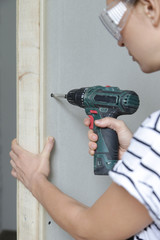 Young woman drilling screws into plasterboard with an electric screwdriver, home improvement concept