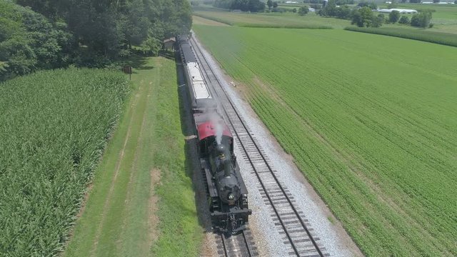 Aerial View of a 1910 Steam Engine with Passenger Train Puffing Smoke Traveling Along the Amish Countryside on a Sunny Summer Day as Seen by a Drone