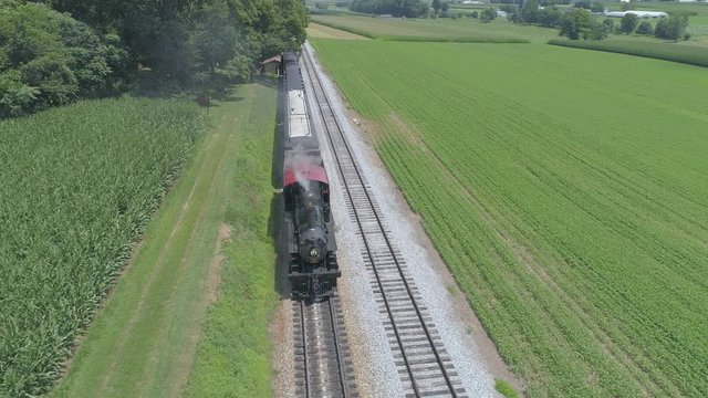 Aerial View of a 1910 Steam Engine with Passenger Train Puffing Smoke Traveling Along the Amish Countryside on a Sunny Summer Day as Seen by a Drone
