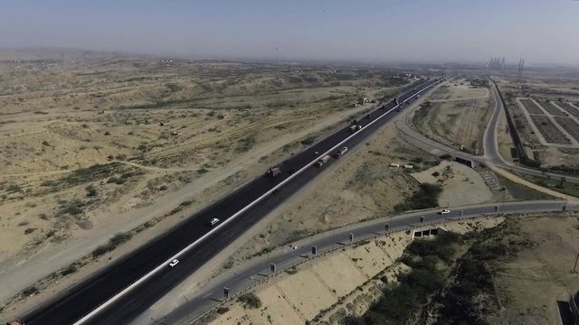 An aerial slow mo view of a highway and city, The heavy trawlers and cars are moving on the highway, an interchange is connecting.