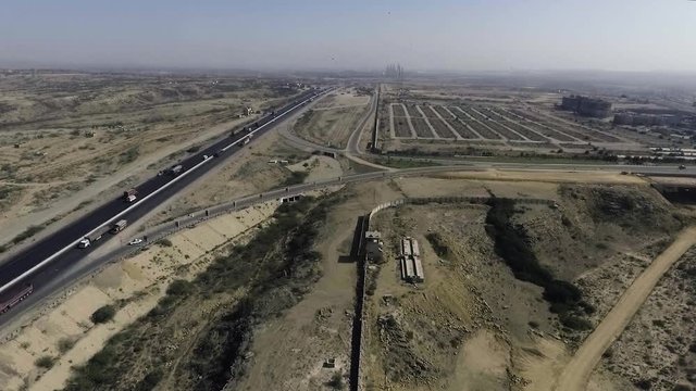 An aerial slow mo view of a highway and city, The heavy trawlers and cars are moving on the highway, an interchange is connecting.