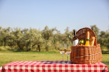 Wicker picnic basket with wine and snacks on table in park. Space for text