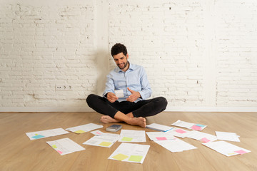 Happy young hipster man sitting on studio home floor calculating own business finance