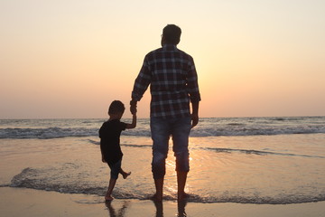 Father and son walking on the beach at sunset