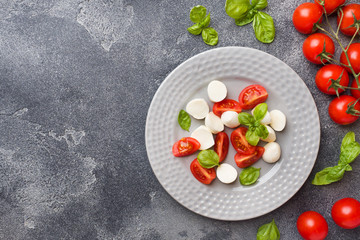 Caprese salad of tomatoes, mozzarella cheese and Basil on a dark background. Italian cuisine. Copy space