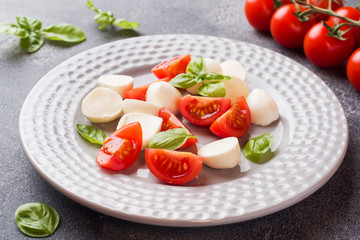 Caprese salad of tomatoes, mozzarella cheese and Basil on a dark background. Italian cuisine.
