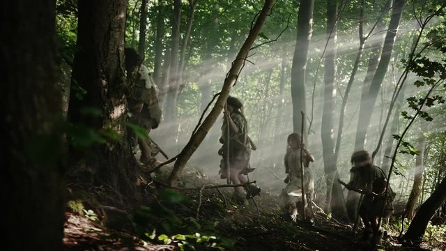 Tribe of Hunter-Gatherers Wearing Animal Skin Holding Stone Tipped Tools, Explore Prehistoric Forest in a Hunt for Animal Prey. Neanderthal Family Hunting in the Jungle or Migrating. Side View