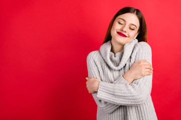 Pretty overjoyed lady with closed eyes touching soft knitted jumper isolated on red background