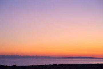 Dawn on a lake in the mountains. rays of the rising sun, orange color. Kyrgyzstan, Issyk-Kul Lake. Bright sky, background in warm colors.