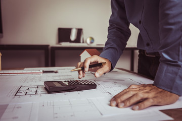 Architect Engineer using calculator Estimate construction drawings with blueprint in construction site.