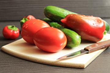 Fresh washed vegetables and a knife lie on a wooden board.