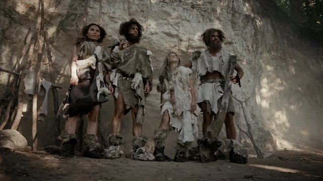 Tribe of Four Hunter-Gatherers Wearing Animal Skin Holding Stone Tipped Tools, Pose at the Entrance of their Cave