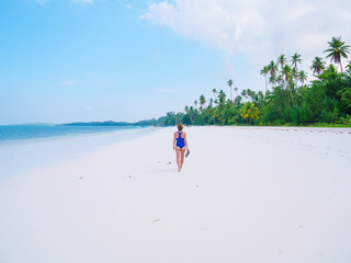 Woman walking on tropical beach. Rear view white sand beach turquoise trasparent water caribbean sea real people. Indonesia Kei Islands Moluccas travel destination.