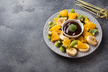 Chocolate fondue with fruit on a dark concrete background. concept summer party. Copy space