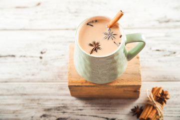 Details of still life in the home interior living room. Beautiful Cup of tea with milk, star anise, cinnamon on a wooden background. Cozy autumn-winter concept. Masala is a traditional hot spicy drink