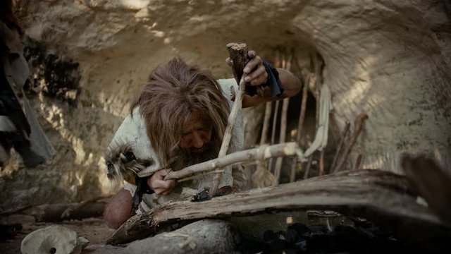 Primeval Caveman Wearing Animal Skin Trying to make Fire with Bow Drill Method. Neanderthal Kindle First Man-Made fire in the Human Civilization History. Making Fire for Cooking. Slow Motion Close-up