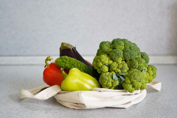 Set of products in a cotton eco bag on a marble table, eggplant, broccoli, tomatoes, peppers, zucchini. The concept of zero waste.