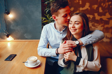 handsome young guy in a blue shirt sitting in a cafe along with her cute girl in a white shirt and they drinking a coffee