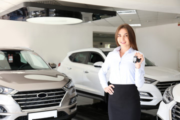 Car dealership sales person at work concept. Portrait of young sales representative wearing formal wear suit, showing vehicles at automobile exhibit center. Close up, copy space, background.