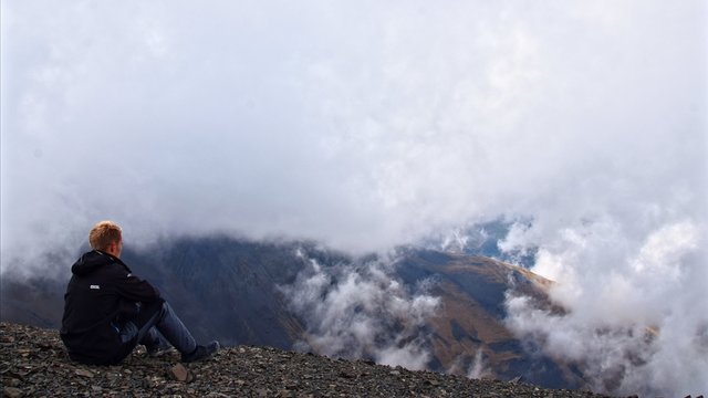 man on top of mountain sitting 16x9