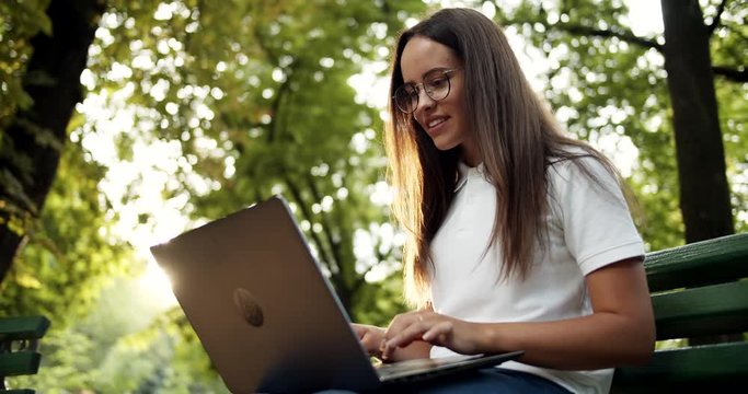 Young female freelancer finishing work and closing laptop, feeling happy and relaxed sitting on bench in park