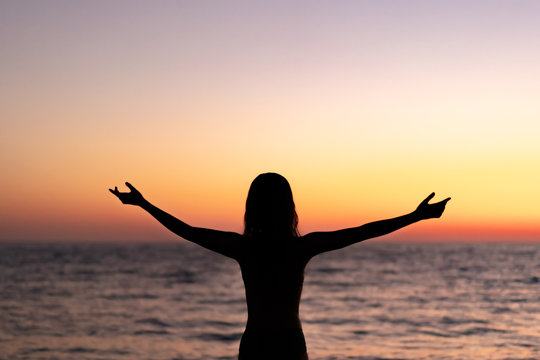 Silhouette of beautiful young gracile pensive woman with a freedom feeling  rise hand up on beautiful sunset. Freedom and travel adventure happy feeling concept.
