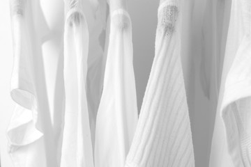 Row of white cotton clothes hang on black hangers on a rack in a shop. Woman minimalist wardrobe. Close-up.