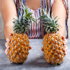 Two halves of ripe pineapple in female hands on gray background.