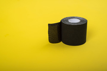 The medical tape lies on a yellow background. Black roll of kineziotape. A sports patch designed to support muscles, joints, and lymphatic drainage.