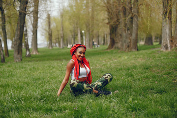 A young and stylish dark-skinned girl with red dreads sitting in the summer park