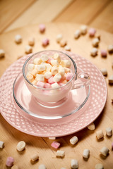Cup with hot milk and colorful marshmallows on wooden table