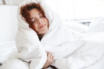 Positive optimistic young lady in lingerie indoors in home hotel lies in comfortable bed.