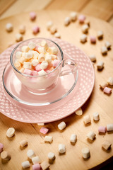 Cup with hot milk and colorful marshmallows on wooden table