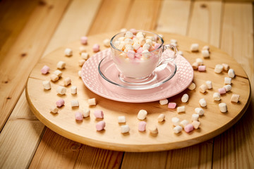 Cup with hot milk and colorful marshmallows on wooden table