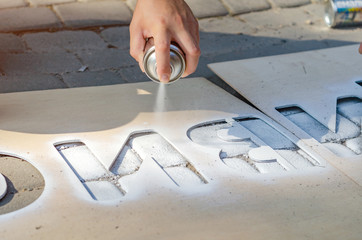 Hand holds an aerosol spray can, puts the image on the asphalt through a stencil