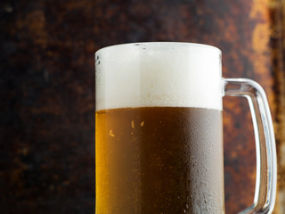 Mug of light beer with drops of water on a dark rusty background