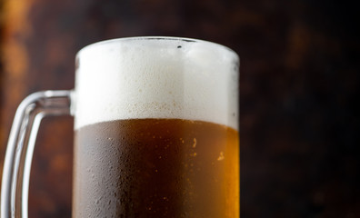 Mug of light beer with drops of water on a dark rusty background